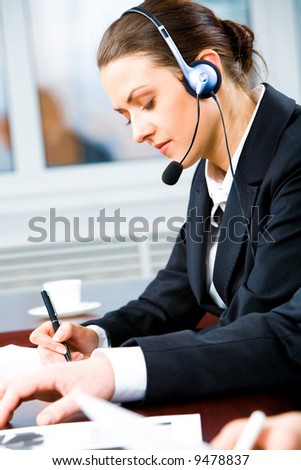Portrait of telephone operator with headset writing something in the office