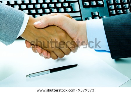 Image of two business people’s handshake after making an agreement on the background of keyboard, pen, paper