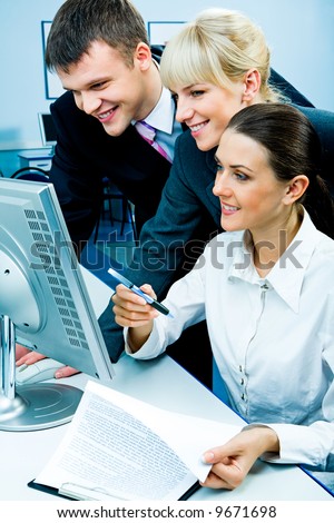 Businessteam of three smiling people looking at the monitor in the computer room