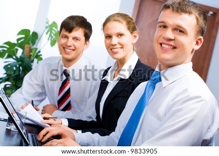 Row of three business people sitting at the table and looking at a camera