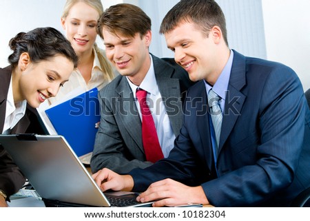 Four business persons gathered together looking at monitor of laptop