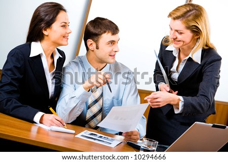 Two smiling business partners looking at confident business lady pointing at document and listening to her idea about new project