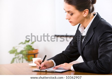 Portrait of serious working businesswoman holding pen in hand and writing something in office