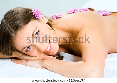 Horizontal photo of a pretty girl lying with flowers on her back and enjoying aromatherapy in the parlor