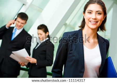 Portrait of cheerful employee in suit holding the folder on the background of business people