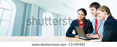 Photo of three office workers sitting at the table on the background of office building