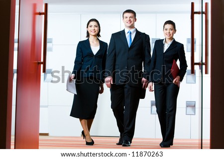 Photo of group of business partners standing in front of open doors and going to enter conference hall