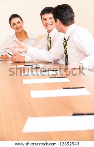 Vertical photo of businessmen discussing new strategy on the background of smiling woman looking at them