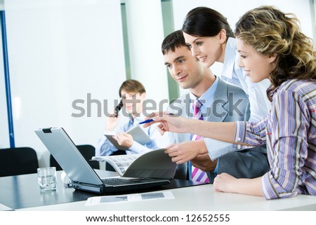 Business-team of several workers looking at the laptop screen on the background of businessman speaking on the phone