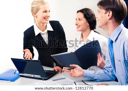 Photo of business lady by the laptop pointing at its monitor and looking at her co-workers with smile