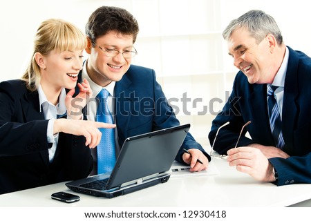 Photo of  business team sitting at the table with laptop on it and looking at its screen while smiling woman pointing at monitor