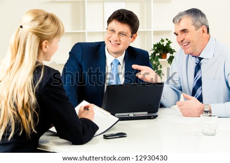 Three business partners discussing new working ideas around table with laptop on it