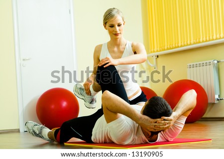 Photo of sportsman doing physical exercise while his pretty instructor helping him in the gym