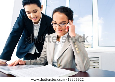 Portrait of business ladies in the office reading business plan and discussing it on the background of window