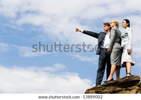 Portrait of business people standing on huge stone while man pointing at something in the distance