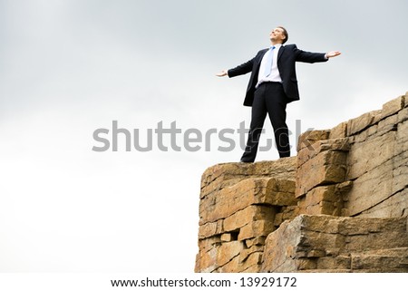 Happy businessman stands on the mountain and enjoys fresh wind