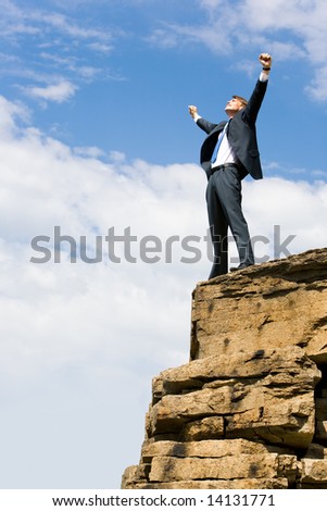 Image of delighted businessman standing on the mount peak with his arms raised