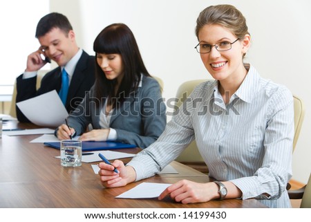 Image of three businesspeople sitting at the table in row with woman looking at camera in front