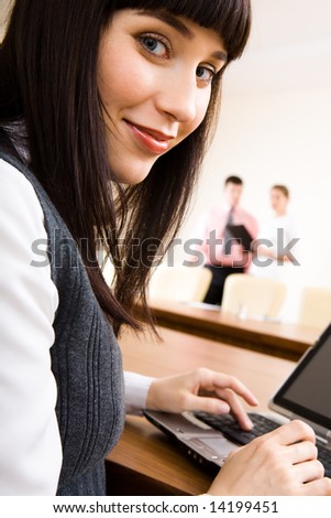 Photo of businesswoman looking at camera during typing a letter on the laptop