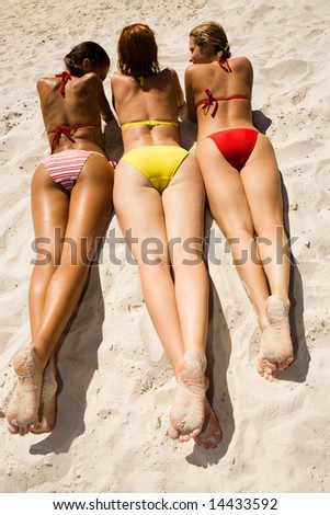 View of pretty girlsâ?? backs lying on the beach and chatting with each other