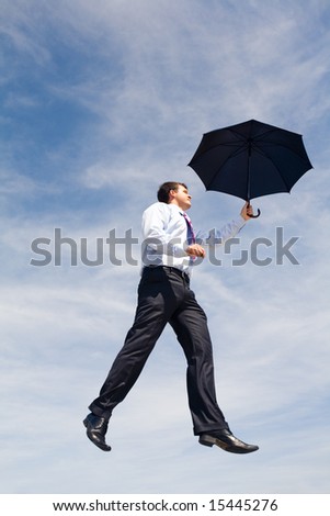 Creative image of businessman with black umbrella flying on the background of sky
