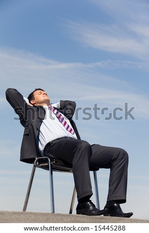 Portrait of sitting businessman with his eyes closed and hands behind head outside at summertime