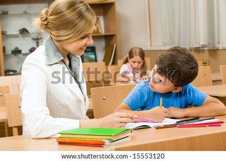 Photo of teacher and schoolboy sitting together at the desk and interacting during lesson