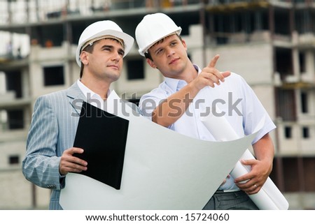 Photo of young engineer showing something to his colleague during meeting at building site