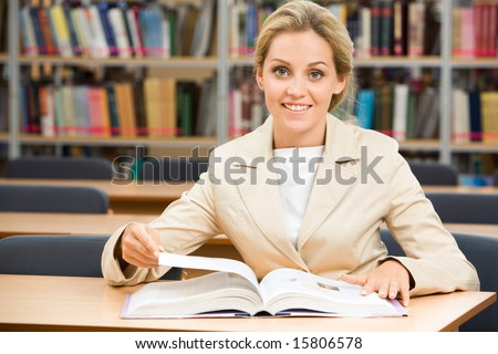 Portrait of happy student sitting in library before textbook and looking at camera