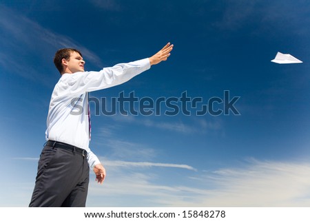 Portrait of handsome man launching paper aircraft into blue sky at summer