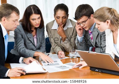 Portrait of confident people looking seriously at business papers during working meeting