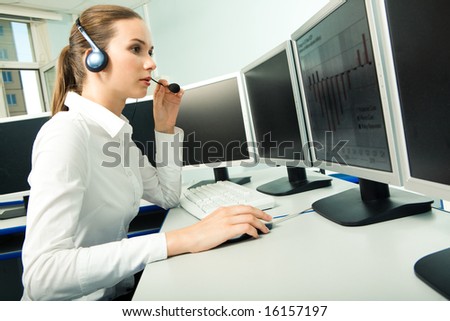 Photo of pretty consultant wearing headset and sitting in front of computer display while consulting client