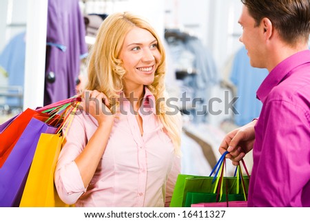 Portrait of happy blond woman looking at smiling man and holding bags in hands
