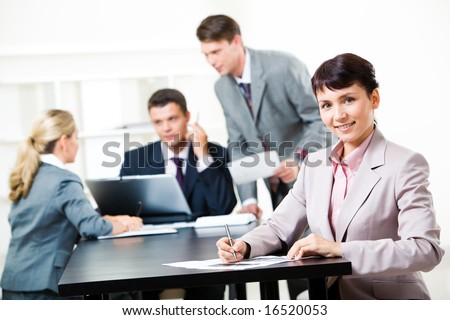Image of confident lady sitting at the table on background of working business team