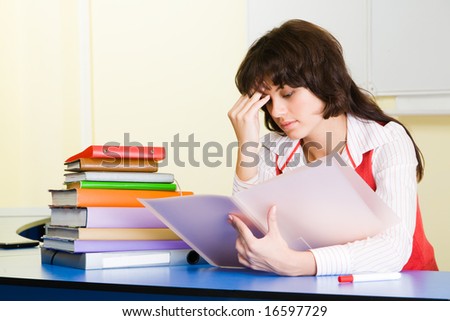 Photo of pensive teacher sitting at the desk and refreshing study material before lesson
