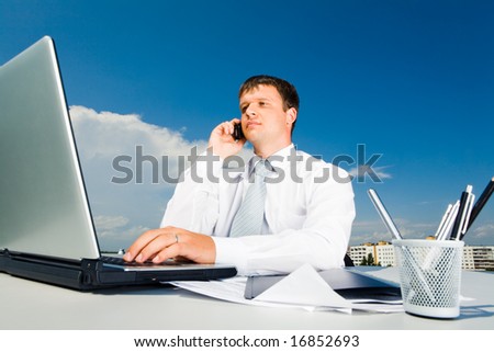 Portrait of confident businessman calling by mobile and typing on the laptop