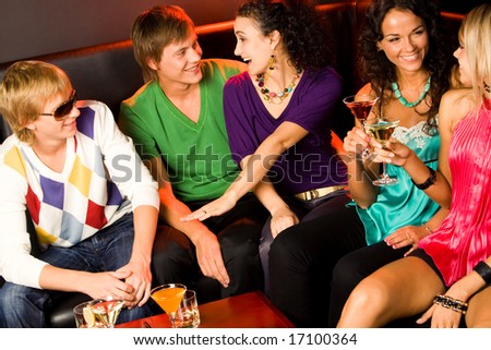 Portrait of five happy people sitting on the sofa and interacting at evening-party