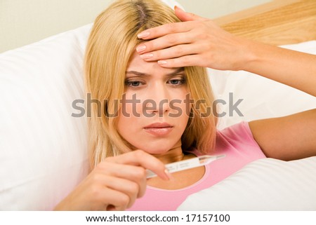 stock photo : Photo of young woman lying in bed and looking at thermometer reading
