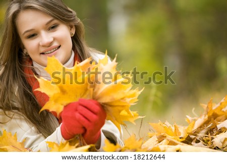 Portrait of beautiful woman holding bouquet of fallen leaves in hands and looking at camera with smile