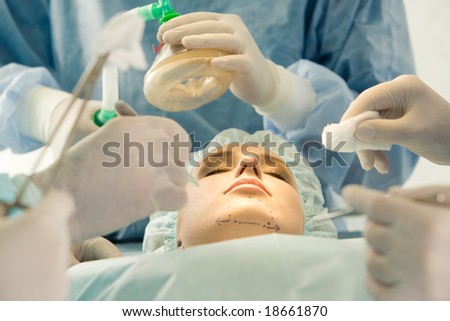 Photo of young female patient lying with closed eyes before operation with hands of doctors over her