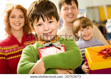Portrait of glad boy with present looking at camera on background of family members