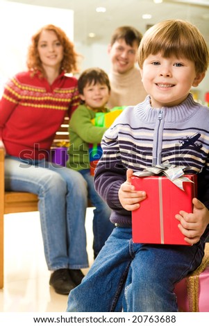 Happy youngster with Christmas present sitting on pink box and looking at camera