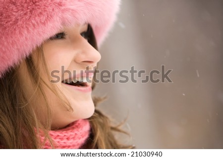 Close-up of happy woman in fashionable fur cap laughing during snowfall