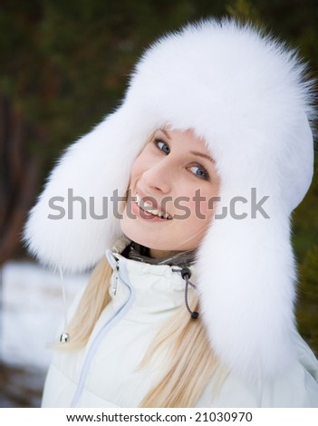 Portrait of fresh woman in white fur cap with ear-flaps and looking at camera with smile