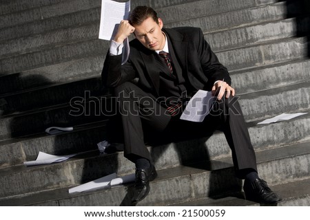 Portrait of sad businessman sitting on stairs with papers in hands and lost expression on his face