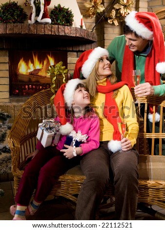 Portrait of happy family wearing santa caps while sitting by fireplace and looking at each other
