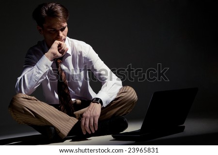 Image of man sitting on floor with laptop in front and looking at its monitor