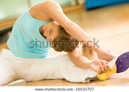 Image of sporty girl sitting on the floor and doing stretching exercise