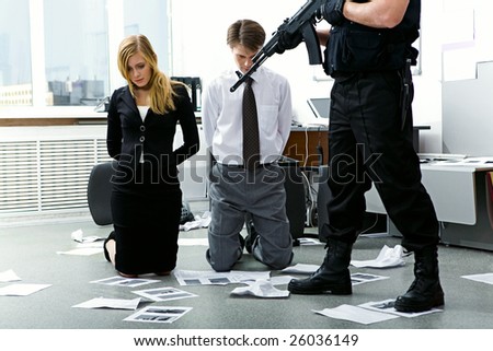 Legs of criminal with gun pointed at scared man and woman in office