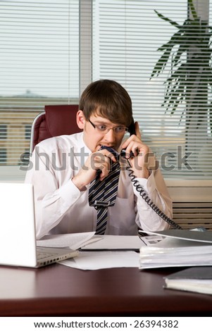 Portrait of scared boss with tie tip in mouth calling by the phone in office